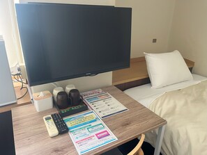 A hotel room with a bed, a TV, a bedside table with a remote control, a tissue box, and a menu. - Hotel Nobeoka Hills (Nobeoka)
