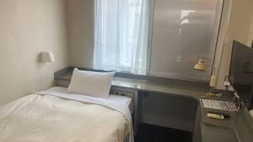 Habitación de hotel con cama, escritorio, silla, ventana con cortinas, lámpara de escritorio y televisor.