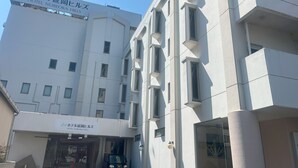 Un hôtel avec une enseigne en japonais et en anglais, une façade moderne et un véhicule garé devant.