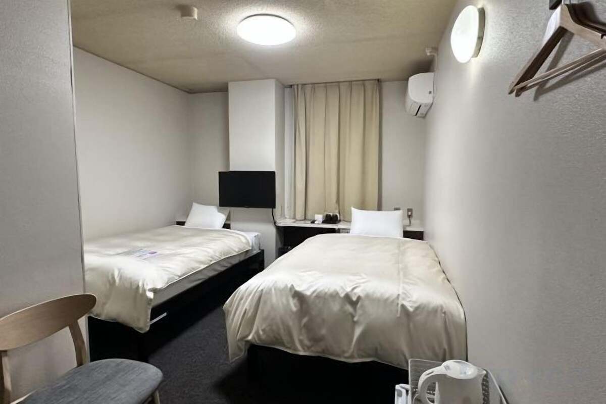 Quarto de hotel com duas camas, uma escrivaninha, uma cadeira, uma televisão e uma janela com cortinas.