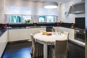 A modern kitchen with a central island, a dining table with chairs, and a window with a view of greenery. - Villa Dei Sassi, Villa by the sea with pool (Ancona)