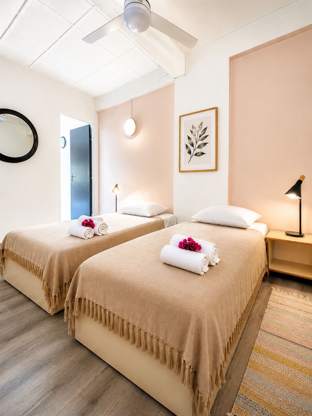 A hotel room with two beds, a ceiling fan, a framed leaf artwork, a bedside lamp, and a mirror.