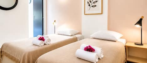 A hotel room with two beds, a ceiling fan, a framed leaf artwork, a bedside lamp, and a mirror.