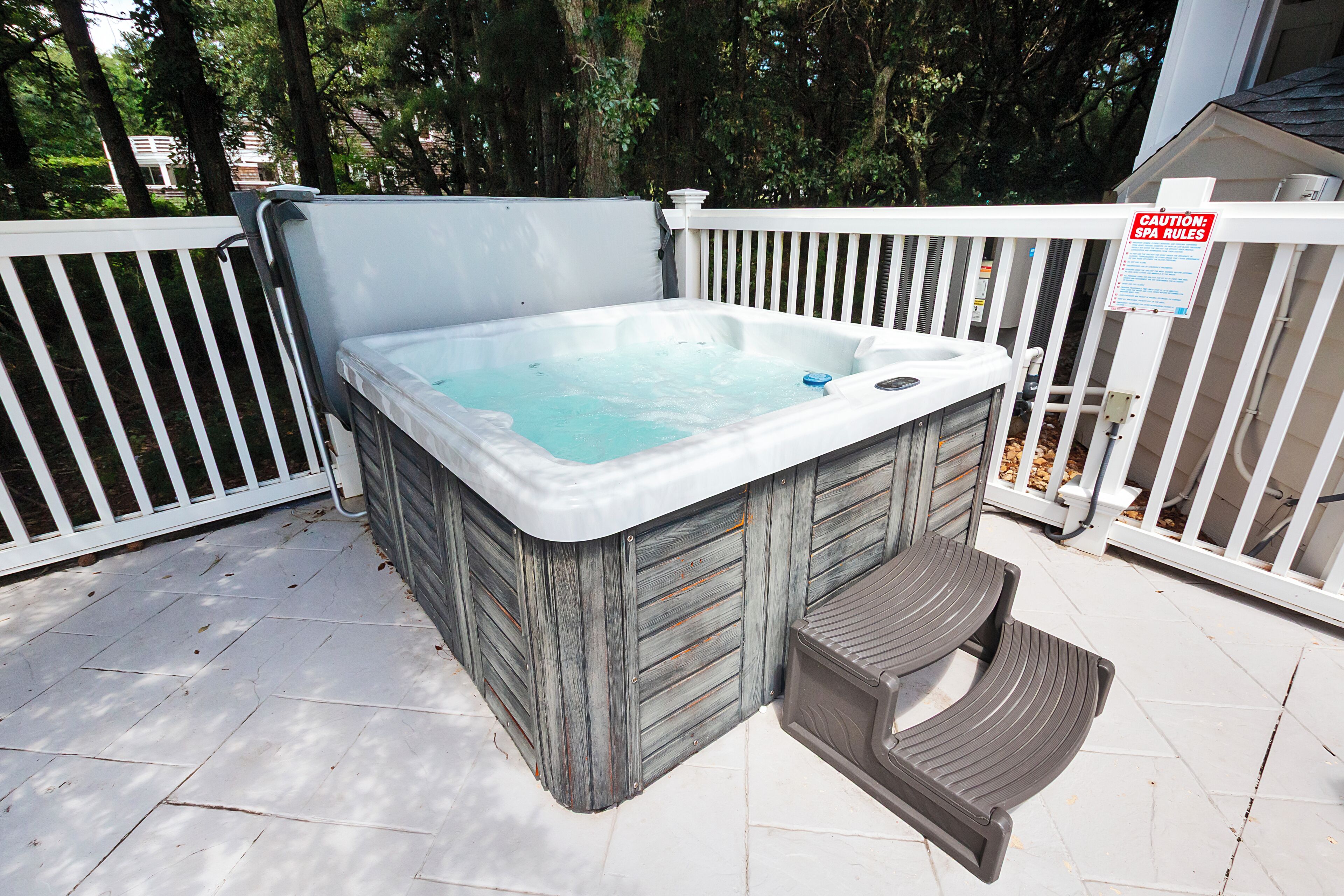 A hot tub with a wooden exterior, a metal ladder, and a caution sign on the fence.