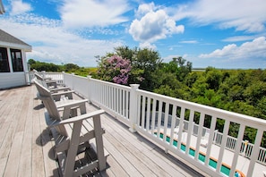 Eine Holzterrasse mit weißen Geländern, ein Schwimmbecken und Blick auf eine natürliche Landschaft.