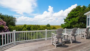 A wooden deck with white railings, outdoor seating, and a view of a green landscape. - Soundside-ELEV, Priv pool, HTub, Rec Rm-CC328, Pipers Perch (Corolla)