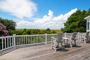 Eine Holzterrasse mit weißen Geländern, Sitzgelegenheiten im Freien und Blick auf eine grüne Landschaft.