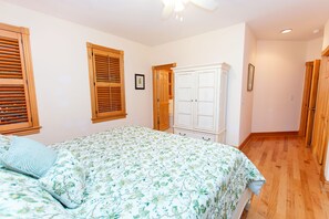 Un dormitorio con una cama, contraventanas de madera, un armario blanco y un pasillo.