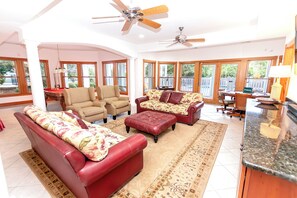 Amplia sala de estar con mesa de billar, múltiples opciones de asientos y grandes ventanas con vistas al exterior.