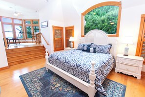 A bedroom with a bed, a nightstand, a lamp, a window with a view of greenery, and a staircase leading to another room. - Soundside-ELEV, Priv pool, HTub, Rec Rm-CC328, Pipers Perch (Corolla)