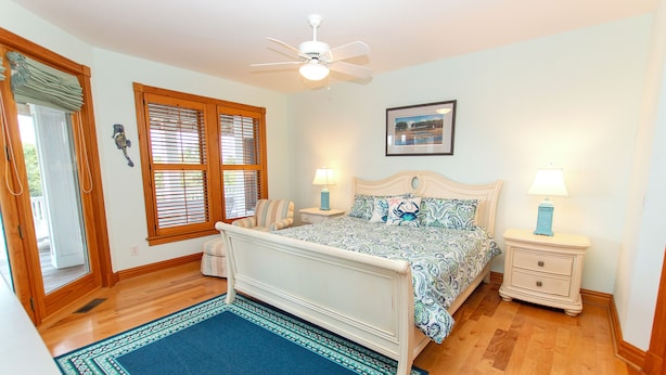 A bedroom with a bed, two bedside tables, a ceiling fan, a window with blinds, a rug, and a framed picture on the wall. - Soundside-ELEV, Priv pool, HTub, Rec Rm-CC328, Pipers Perch (Corolla)