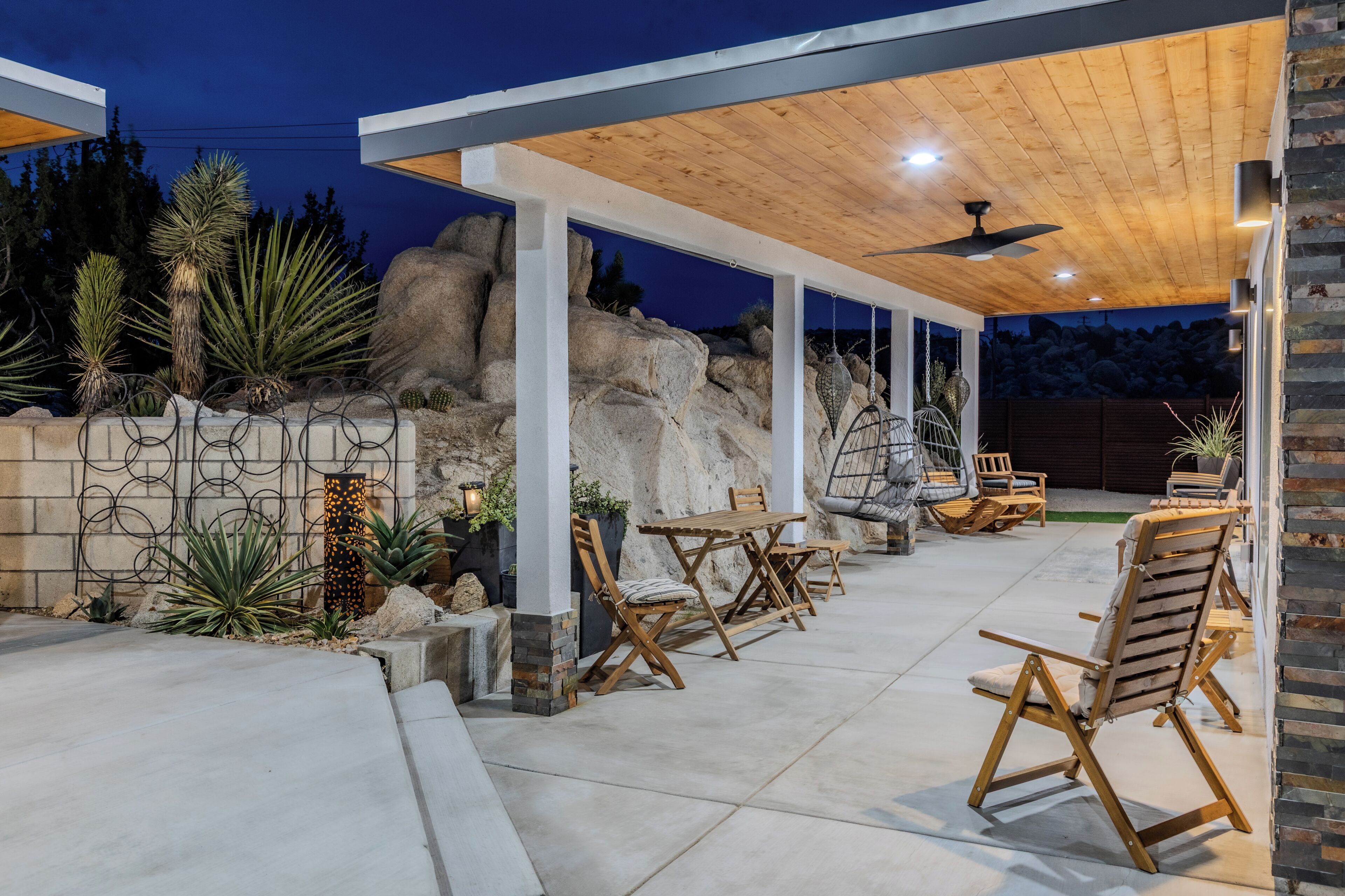 An outdoor patio area with wooden furniture, a stone wall, and a view of the surrounding landscape.