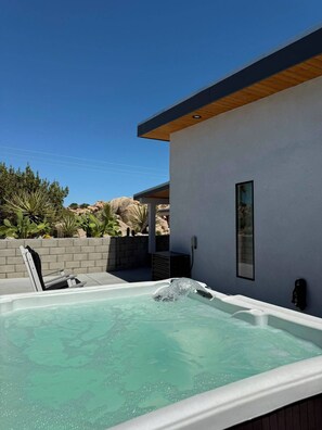 Un espace moderne aménagé à l’extérieur avec un bain à remous, offrant une vue dégagée sur le ciel et la végétation environnante.
