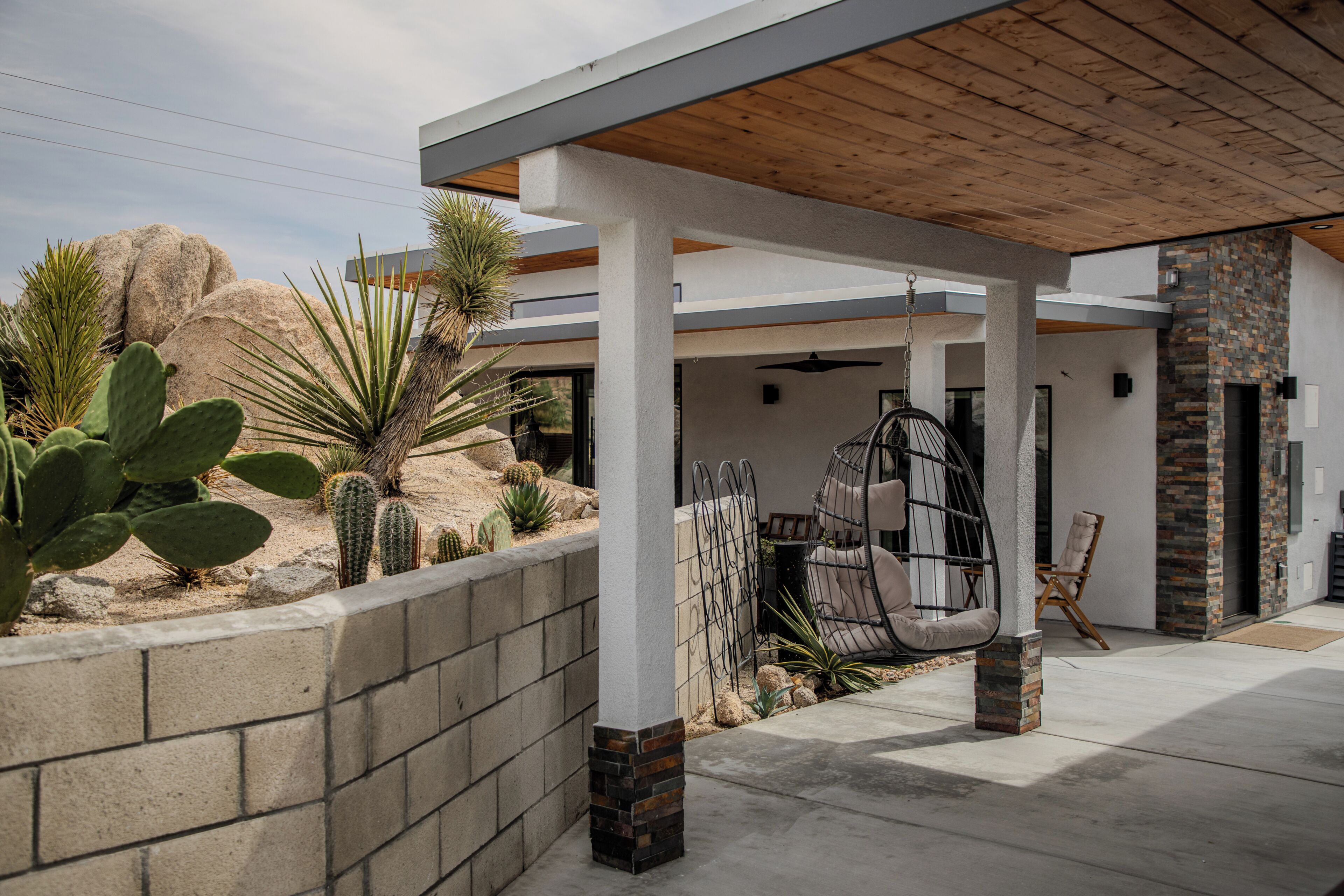 A covered outdoor area with a hanging chair, a cushioned bench, and a stone fireplace.