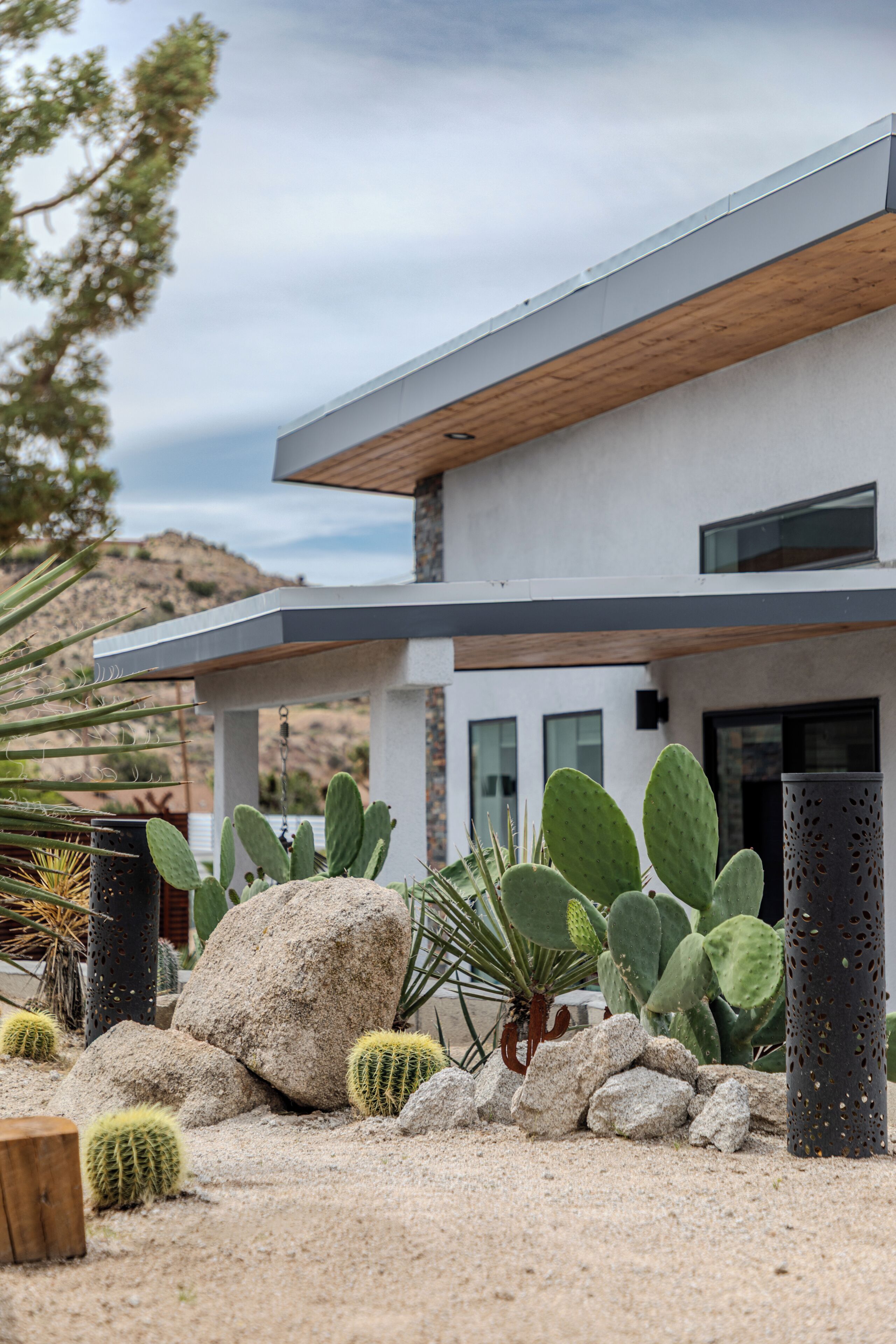 A modern house with a flat roof, large windows, and a garden with various cacti and rocks.