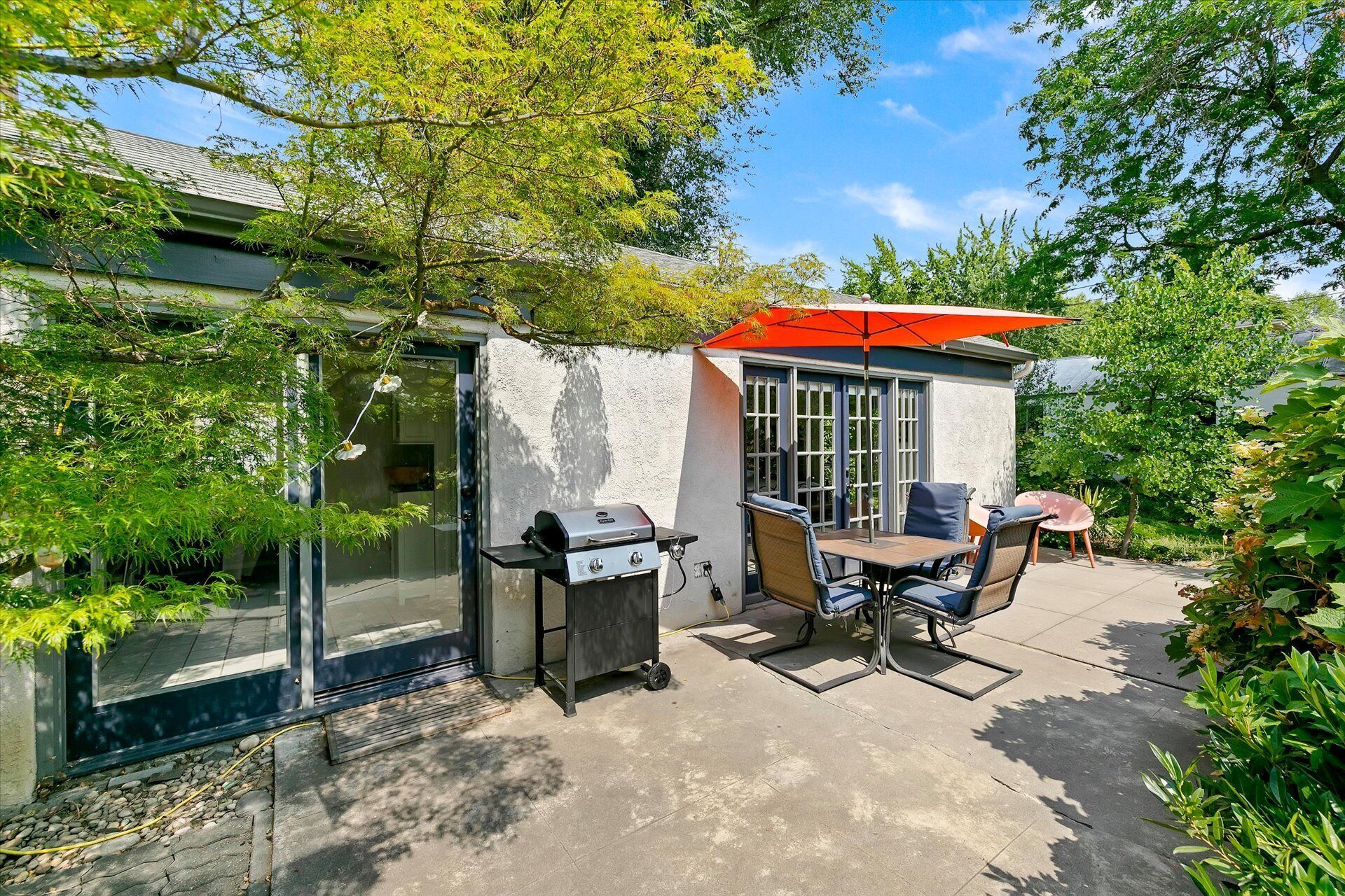 An outdoor patio with a grill, seating, and a red umbrella.