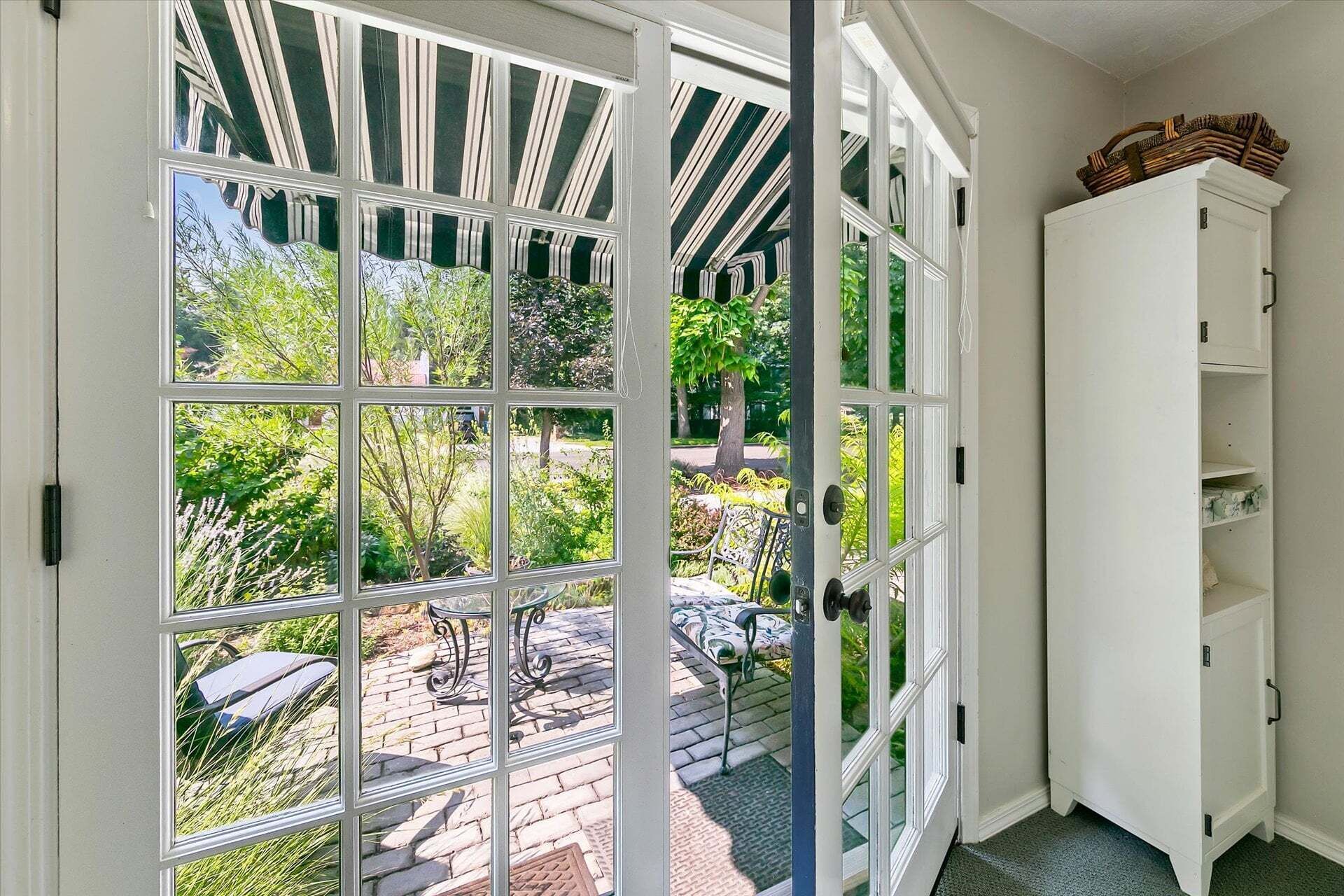 Une pièce donnant sur un jardin grâce à une porte vitrée, avec un meuble blanc et un plafond orné de motifs.