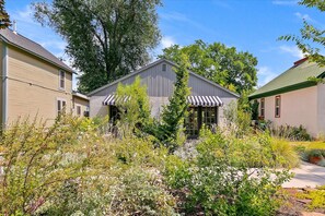 A residential property with a central building featuring a porch and a garden in the foreground. - #HabitueHomes - Jeanette's Retreat (Boise)