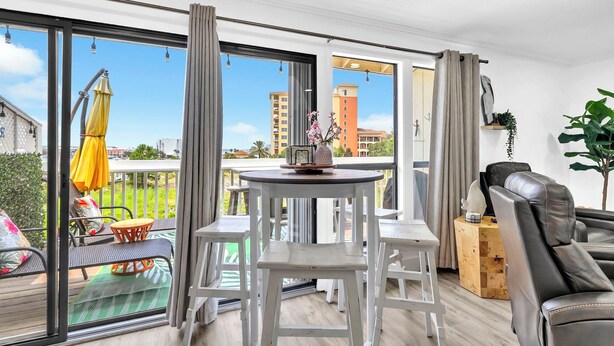 A modern living room with a dining area, large sliding glass doors, and a view of the cityscape. - Sandpiper Cover 2020 - Near Beach - Sleeps 4 (Destin)