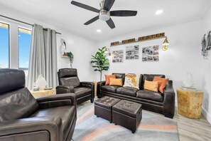 A modern living room with leather sofas, a coffee table, a ceiling fan, and a wall with framed photographs. - Sandpiper Cover 2020 - Near Beach - Sleeps 4 (Destin)