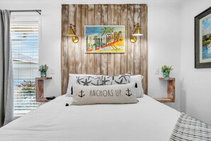 A bedroom with a bed, two bedside tables, a window with blinds, a wooden headboard, and a painting. - Sandpiper Cover 2020 - Near Beach - Sleeps 4 (Destin)