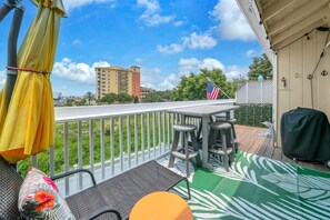 A covered outdoor area with a table and chairs, a grill, and a view of a building in the background. - Sandpiper Cover 2020 - Near Beach - Sleeps 4 (Destin)