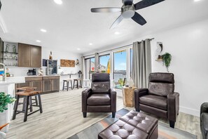A spacious living area with a kitchen, two leather armchairs, a coffee table, and a ceiling fan. - Sandpiper Cover 2020 - Near Beach - Sleeps 4 (Destin)