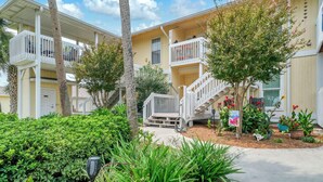A multi-story residential building with balconies, a central staircase, and a well-maintained garden with various plants and flowers. - Sandpiper Cover 2020 - Near Beach - Sleeps 4 (Destin)