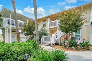 A multi-story residential building with balconies, a central staircase, and a well-maintained garden with various plants and flowers. - Sandpiper Cover 2020 - Near Beach - Sleeps 4 (Destin)