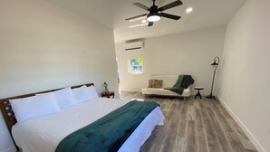Ein Schlafzimmer mit einem großen Bett, einem Deckenventilator, einem Fenster mit Ausblick, einer Couch und einer Stehlampe.