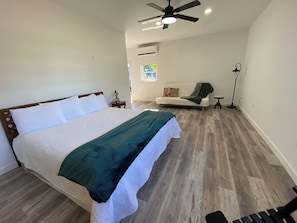 Ein Schlafzimmer mit einem großen Bett, einem Deckenventilator, einem Fenster mit Ausblick, einer Couch und einer Stehlampe.