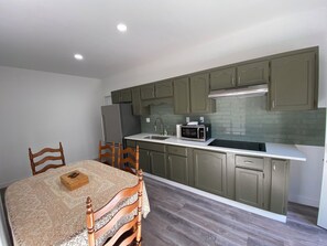A compact kitchen with a dining table, chairs, a refrigerator, a microwave, and green cabinets.