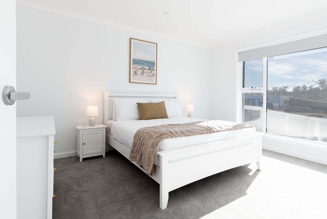 Une chambre à coucher avec un lit, des tables de chevet, une commode, une fenêtre et un tableau encadré au mur.