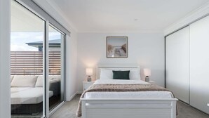 A bedroom with a bed, bedside lamps, a picture on the wall, and a sliding glass door leading to an outdoor area. - Wake Up to Stunning Tamar Valley Views (Riverside)