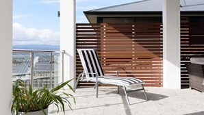 A balcony with a view of the city, a striped lounge chair, and a potted plant. - Wake Up to Stunning Tamar Valley Views (Riverside)