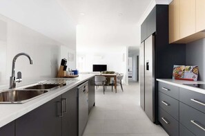 A modern kitchen with a central island, stainless steel appliances, and a dining area in the background. - Wake Up to Stunning Tamar Valley Views (Riverside)