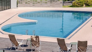 Ein Schwimmbecken mit gewölbter Kante, umgeben von Liegestühlen und einer Liegefläche.