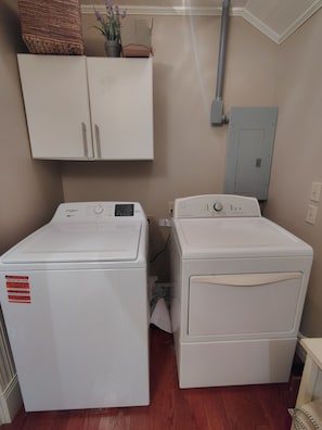 A laundry room with two white Whirlpool washers, a cabinet above, and a utility box on the wall.