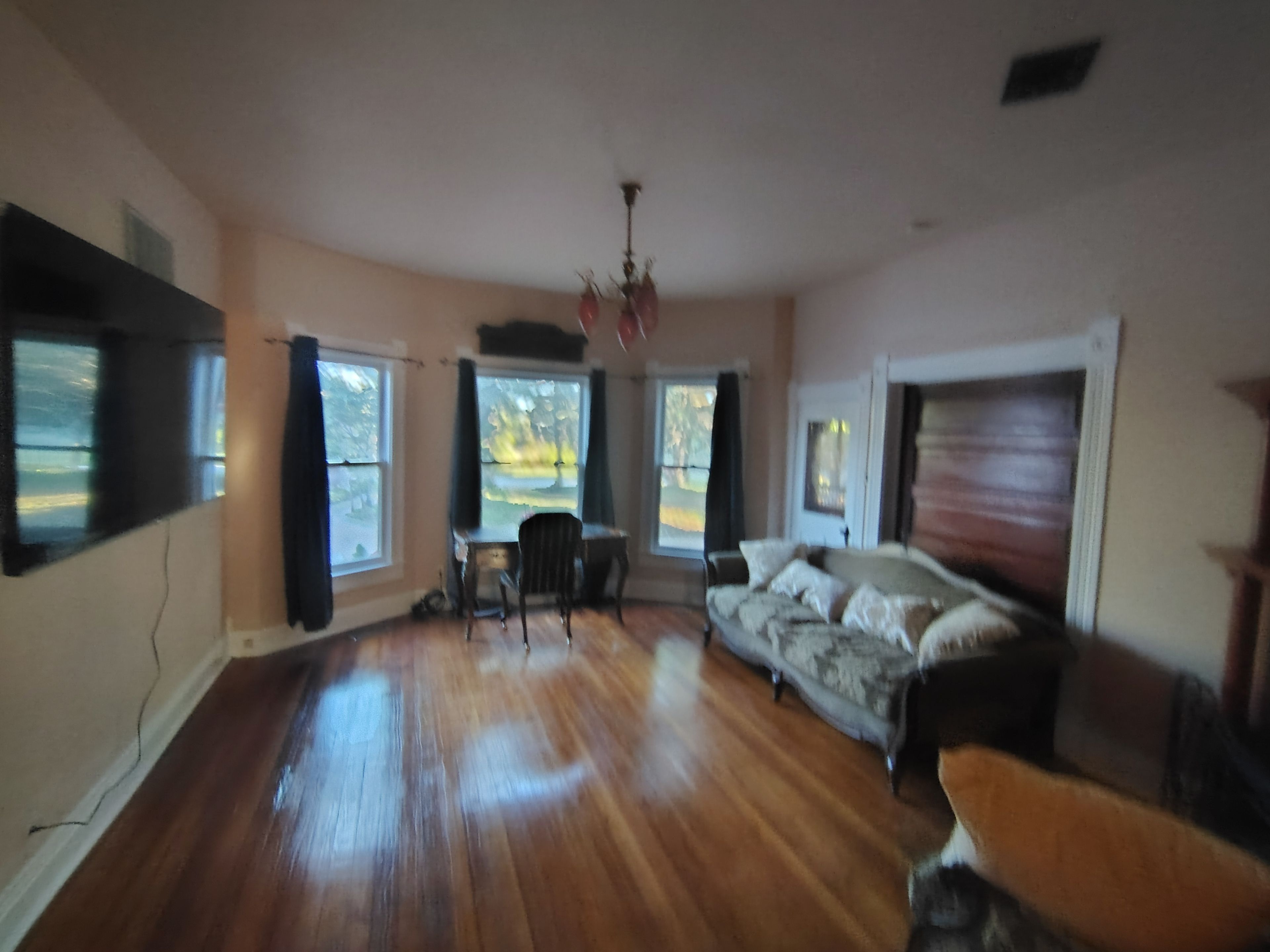Uma sala de estar espaçosa com piso de madeira, um sofá, uma mesa de jantar com cadeiras e janelas amplas.