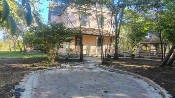 Um pátio pavimentado com um gazebo, rodeado por árvores e uma casa.