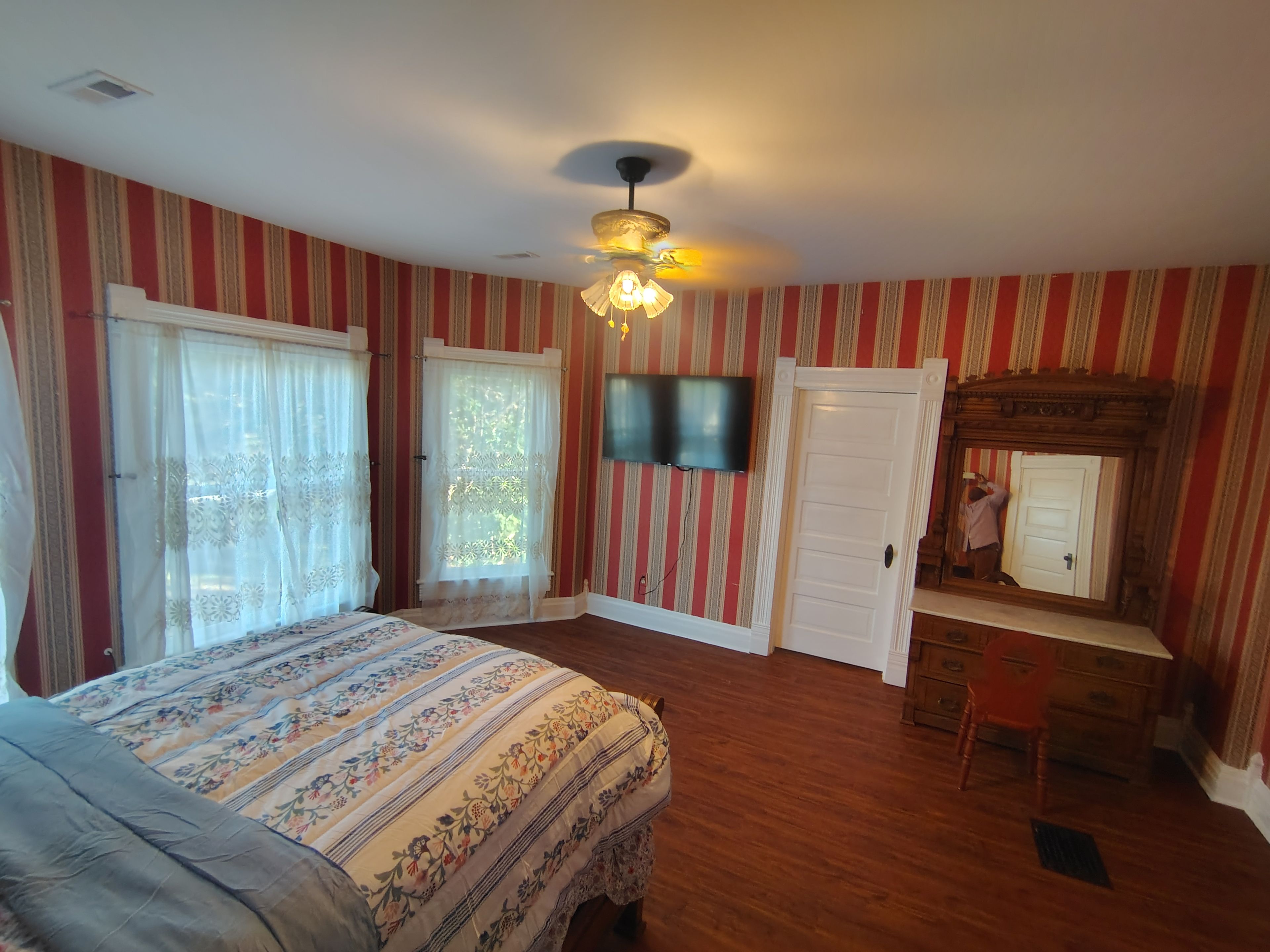 A bedroom with a bed, a ceiling fan, a TV, a mirror, and a door.