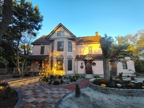 A two-story house with a front porch, a small garden, and a brick pathway leading to the entrance.
