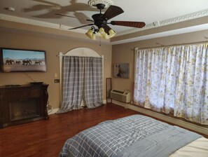 A bedroom with a bed, a ceiling fan, a fireplace, a television, and curtains.