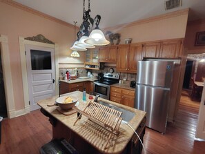 A kitchen with wooden cabinets, a stainless steel refrigerator, a sink, and a wooden drying rack.