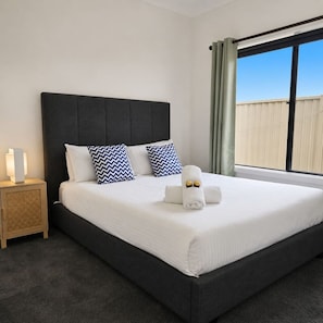 A hotel room with a large bed, a nightstand, a window with curtains, and a view of the outside.