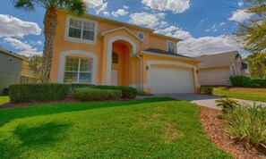 A two-story house with a garage, a well-maintained lawn, and a palm tree. - 648 - Spacious 6-Bedroom Emerald Island Retreat with Pool, Spa & Games Room Near Disney (Kissimmee)