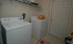 A laundry area with two white washing machines, a shelf with various items, and a door. - 648 - Spacious 6-Bedroom Emerald Island Retreat with Pool, Spa & Games Room Near Disney (Kissimmee)