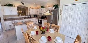 Een moderne keuken met witte kasten, een centraal eiland en een eethoek met een houten tafel voor vier personen.
