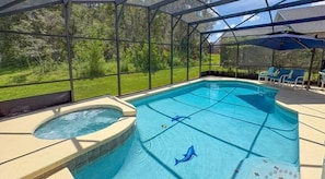 Piscina techada con un jacuzzi, rodeada por un recinto de vidrio y vista a un paisaje verde.
