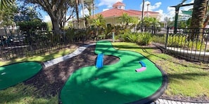 Een minigolfbaan met een groen speeloppervlak, een blauw doel en een roze en blauw obstakel.